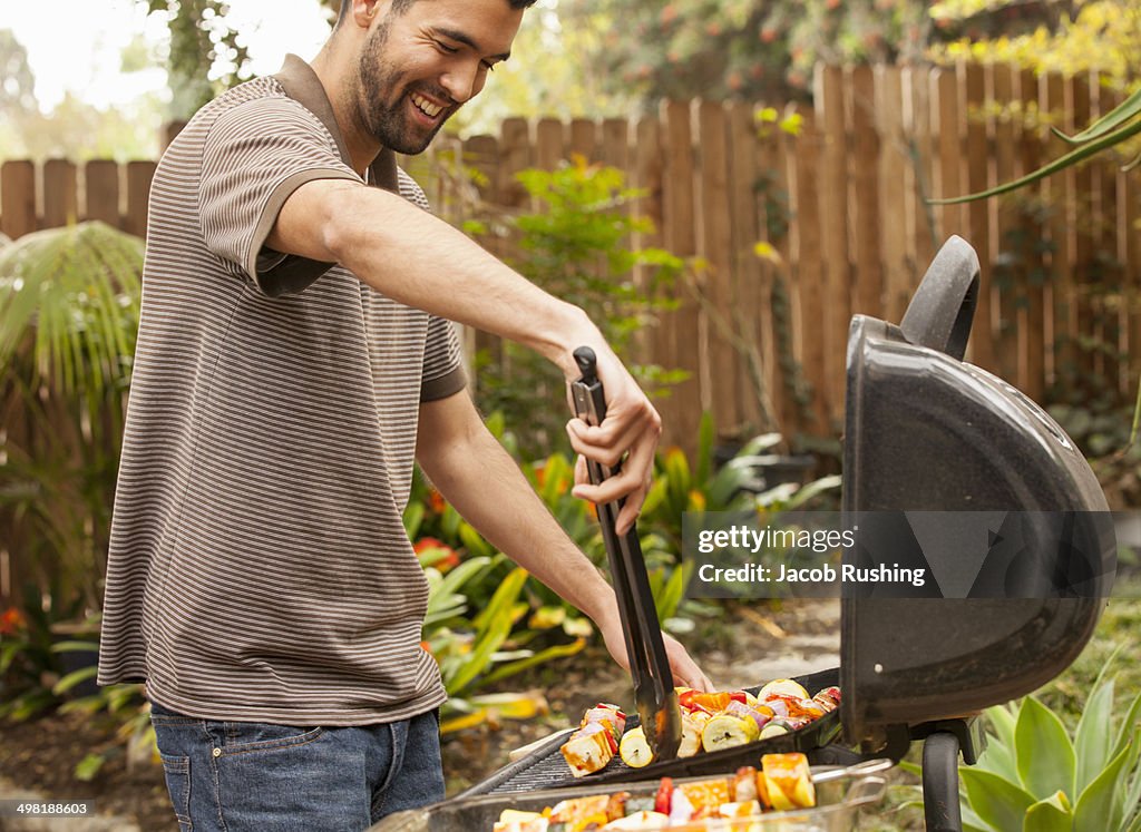 Man cooking vegetable skewers on barbecue