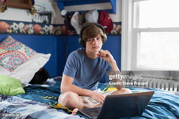 teenage boy sitting on bed with laptop computer - boys bedroom stock-fotos und bilder