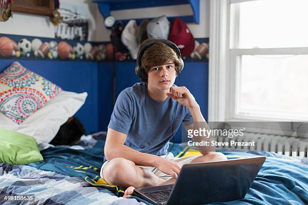 teenage boy sitting on bed with laptop computer - one teenage boy only stock pictures, royalty-free photos & images