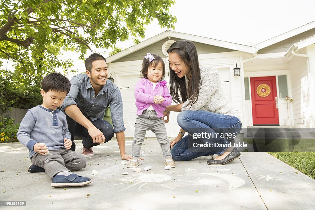 Mid adult couple with two children drawing on paving slabs