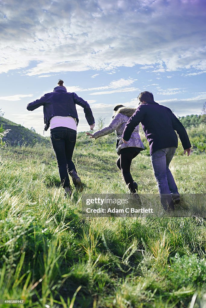Three young adult friends running up grassy hill