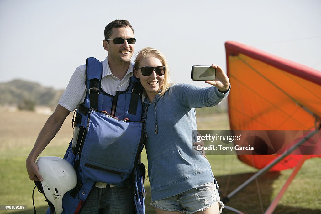 Couple taking selfie, hang glider in background