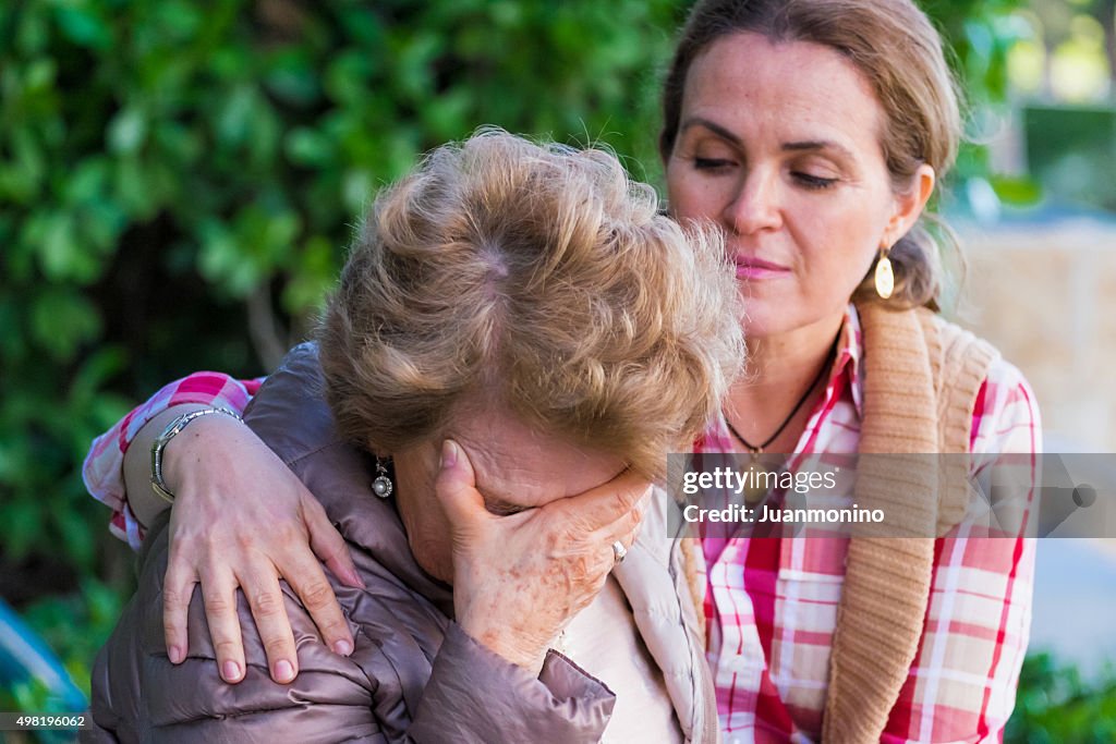 Crying senior woman holding her face being comforted