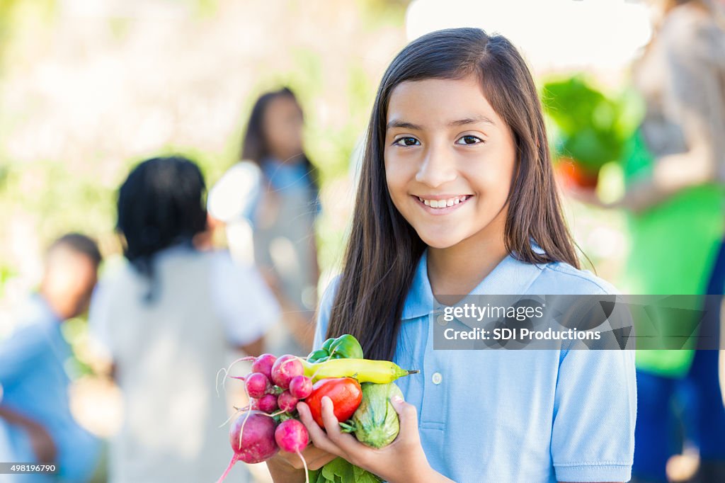Student holding vegetables she picked from garden during field trip
