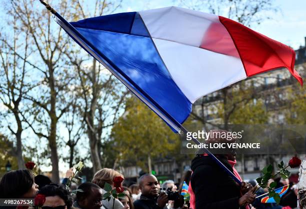 One of several women holding flags of France, the EU and Democratic Republic of the Congo, walks to lay a rose at Place de la Republique in Paris on...