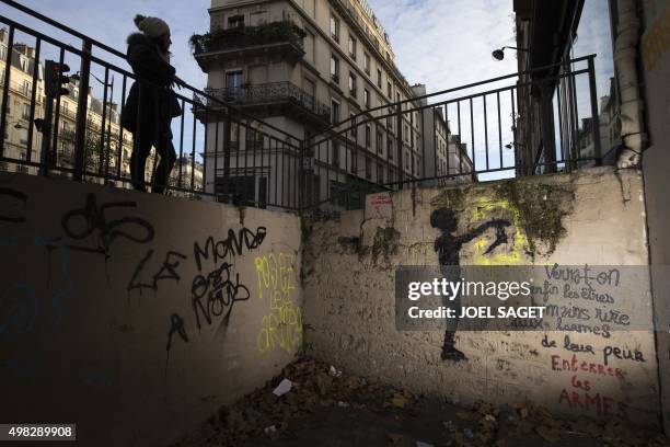 Woman walks past a painting and graffitis which translate as "The world is our", "Put weapons down", "Buried weapons" and "Will we finally see humans...