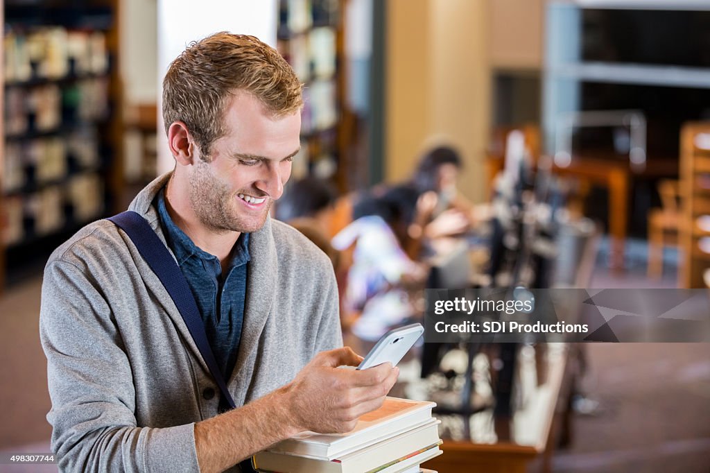 Estudante usando telefone inteligente ao verificar os livros da biblioteca