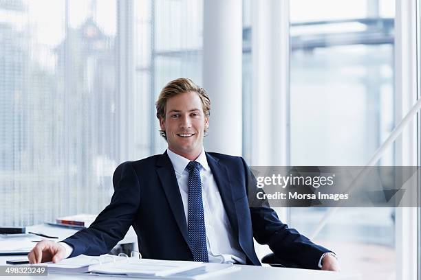 handsome businessman sitting at desk - blaue jacke stock-fotos und bilder