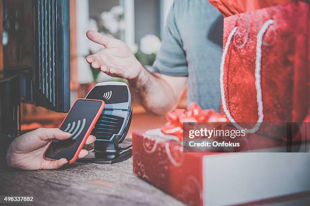 woman paying with nfc technology on smart phone in store - digital devices beside each other stockfoto's en -beelden