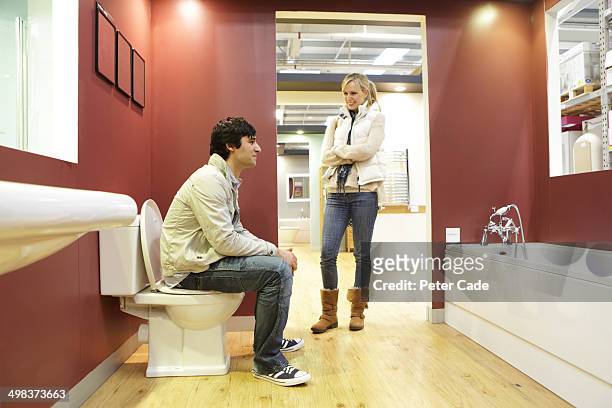 coule in bathroom showroom, man sat on toilet - koppel toilet stockfoto's en -beelden