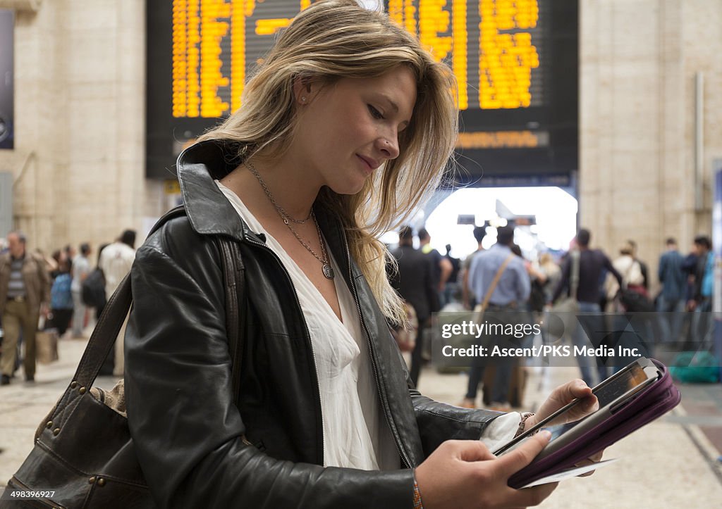 Young woman consults digital tablet, train station