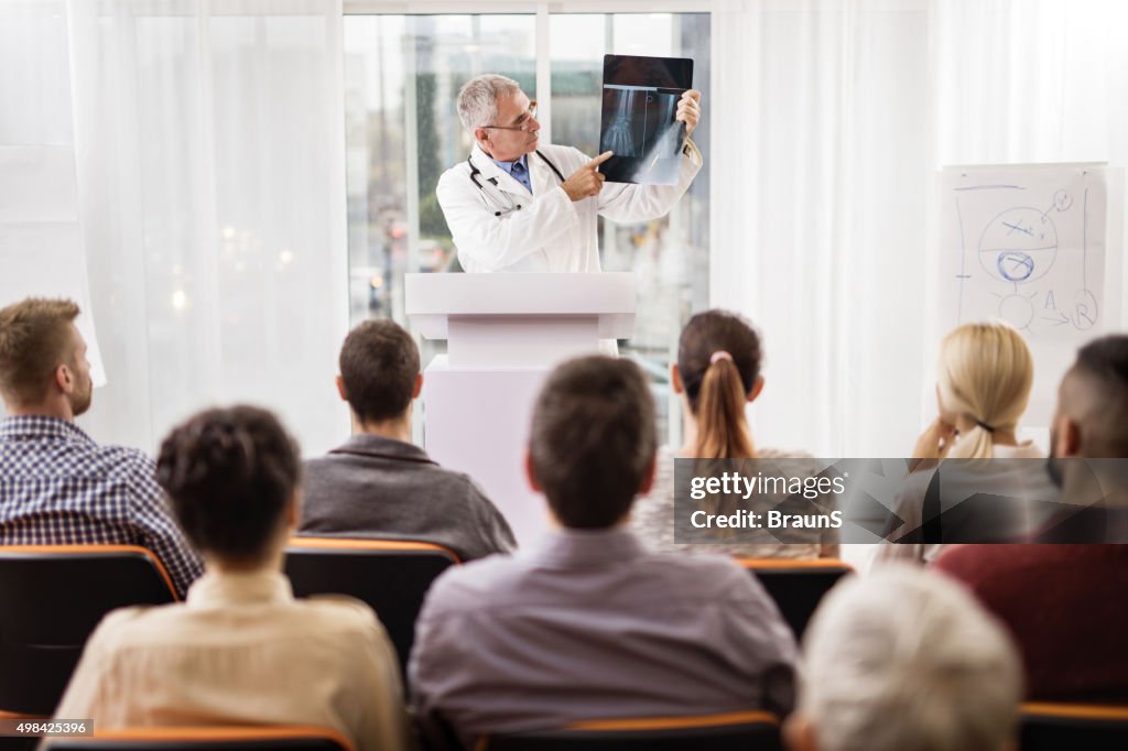 Mature doctor analyzing an X-ray image on education event.