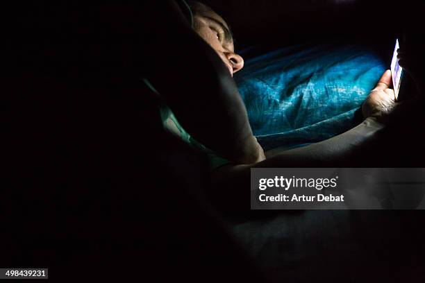 Man laying on bed at late night in a dark room checking his smartphone. Internet addiction.