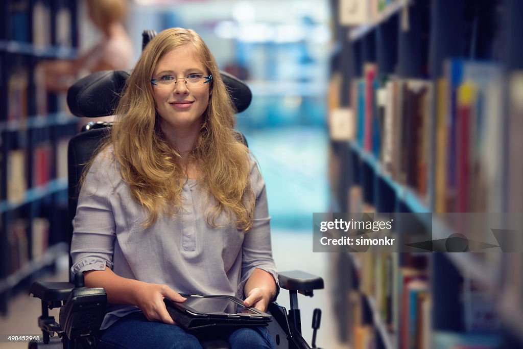 Portrait of young woman in wheelchair in library