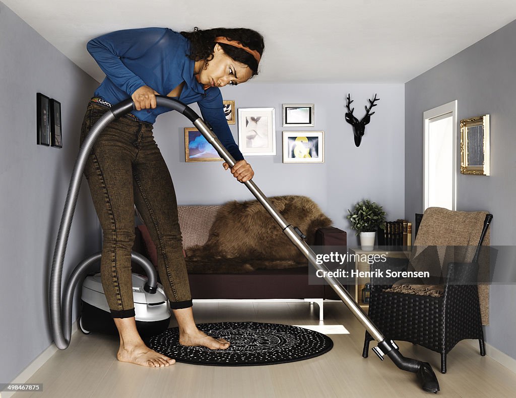 Woman vacuum cleaning in smallscale living room