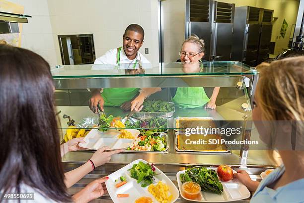einladende cafeteria worker serviert gesunde speisen zur high school-schüler - kantinenfrau stock-fotos und bilder