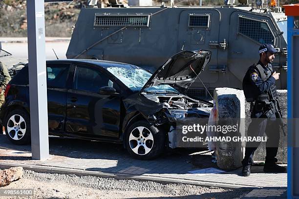 An Israeli policeman stands in front of a damaged car at the spot where a Palestinian man was shot by Israeli forces after reportedly ramming a...