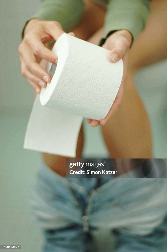 Woman on toilet holding spool of toilet paper