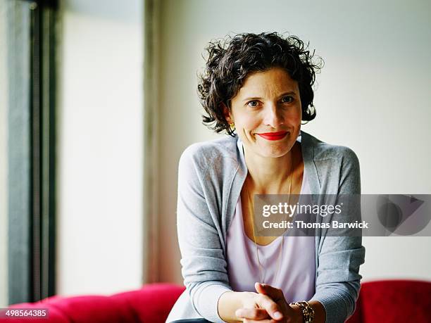 smiling businesswoman leaning against chair - schwarzes haar stock-fotos und bilder