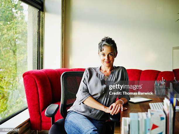 smiling female business owner sitting at desk - middle age woman seated stock pictures, royalty-free photos & images