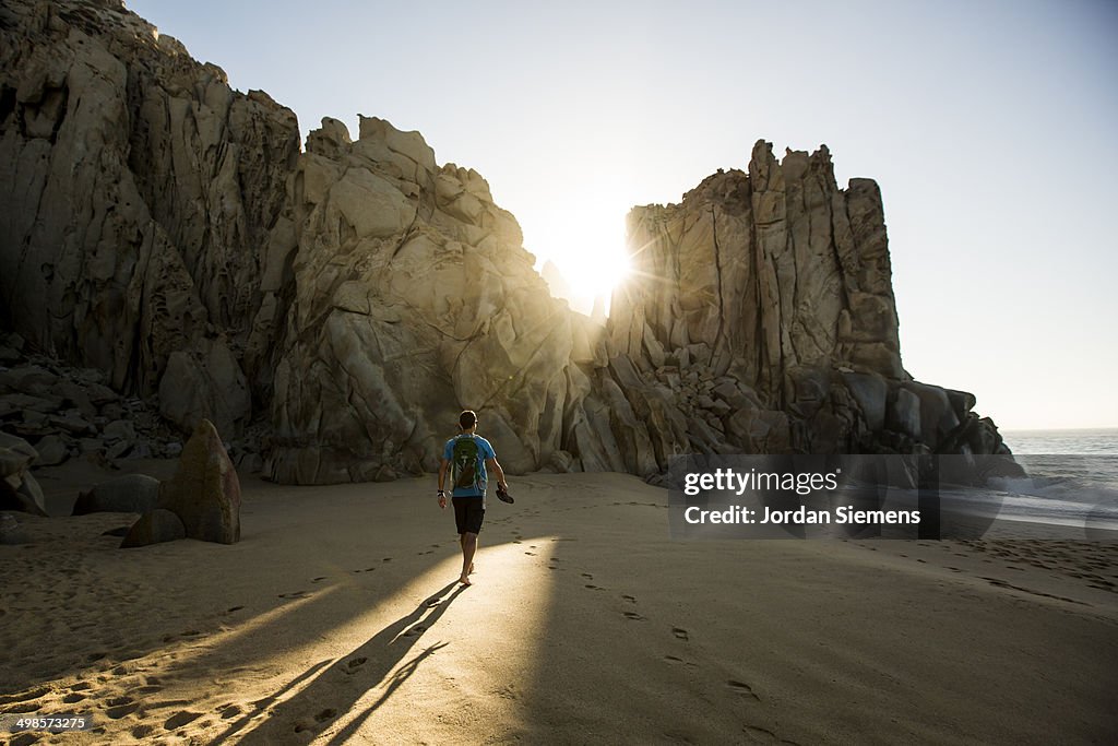 A man walking a beach at sunrise.