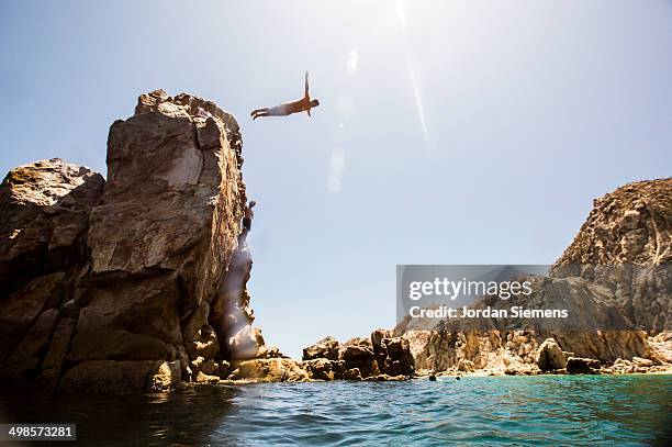 a man diving off a cliff. - cabo san lucas stock-fotos und bilder