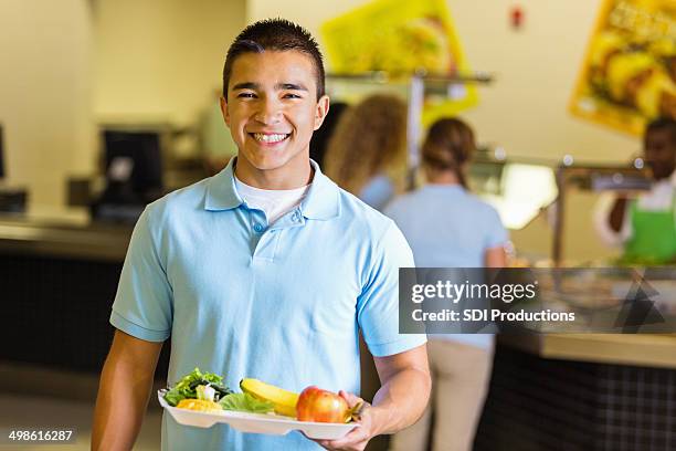 happy student holding tray of healthy food in school lunchroom - school lunch stockfoto's en -beelden