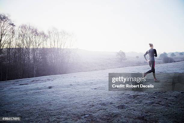 Female Runner Running Through Frosty Misty Field, Stock-Foto