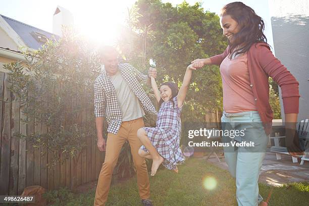 parents swinging their daughter in garden - father sun stock pictures, royalty-free photos & images