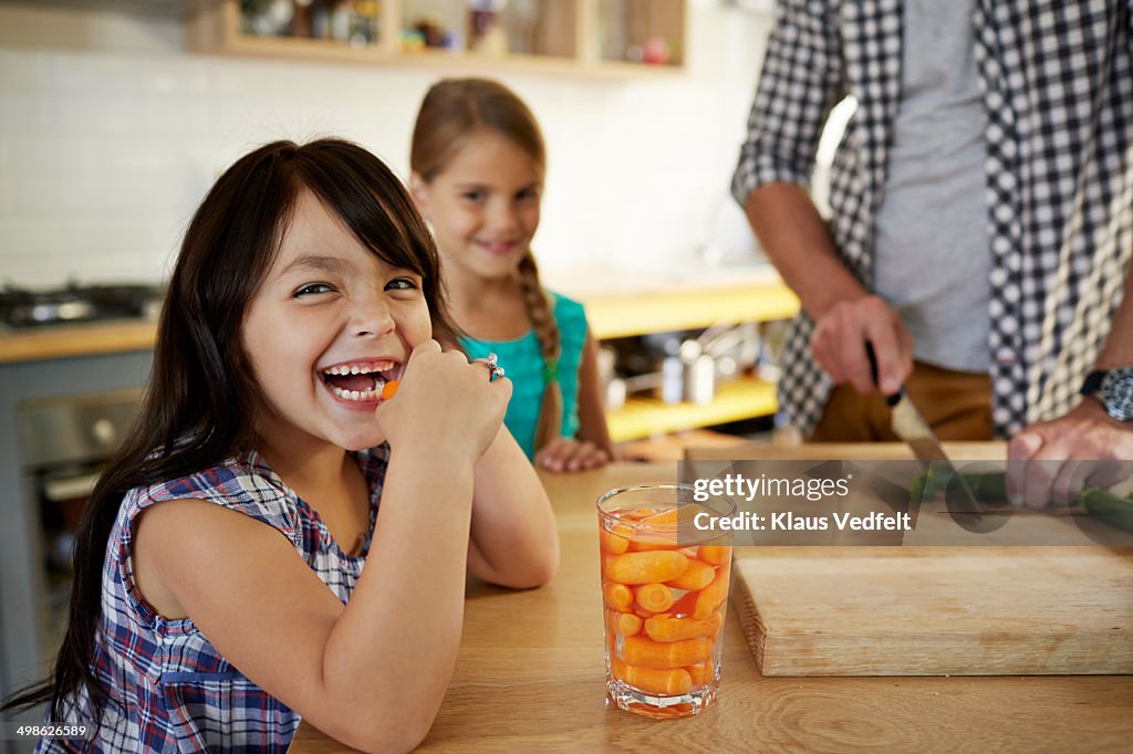 Cute girl eating baby carrots in kitchen