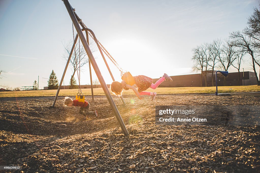 Little kids swinging on swing set on stomach