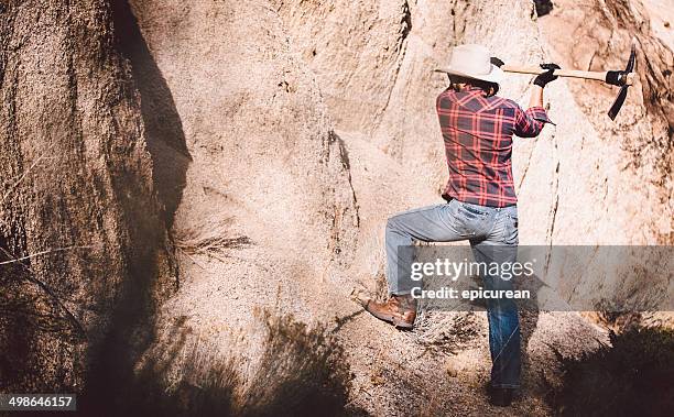 rugged man uses pickaxe against rock face - pickaxe stock pictures, royalty-free photos & images