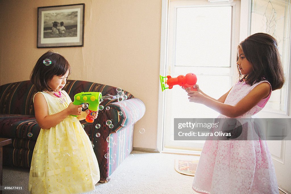 Girls pointing bubble machines at each other