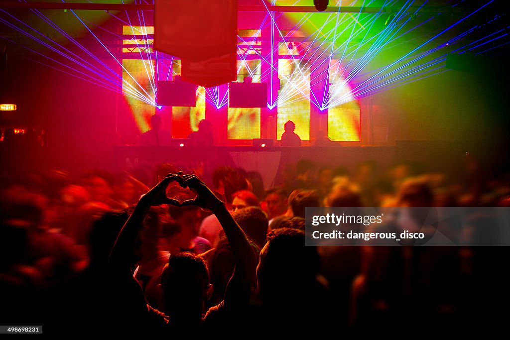 Boy making a heart shape with hands in busy club