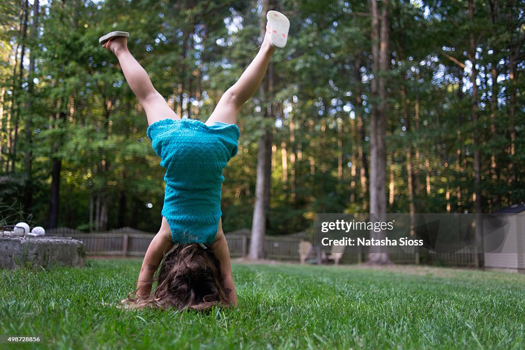 Young girl in a blue dress doing handstands in the backyard