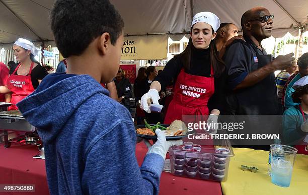 Actress Emmy Rossum serves food to a young boy at the Thanksgiving lunch for homeless outside the Los Angeles Mission in the city's Skid Row during...