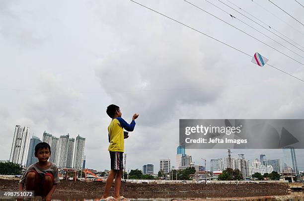 Children play with kites as the skyline of the main business district is partially visible in the background on November 24, 2015 in Jakarta,...