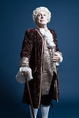 Retro baroque man with white wig standing with walking stick.
