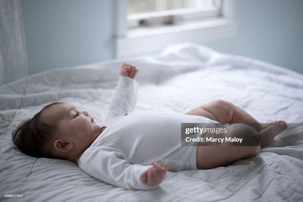 Baby girl lying on a bed in white.