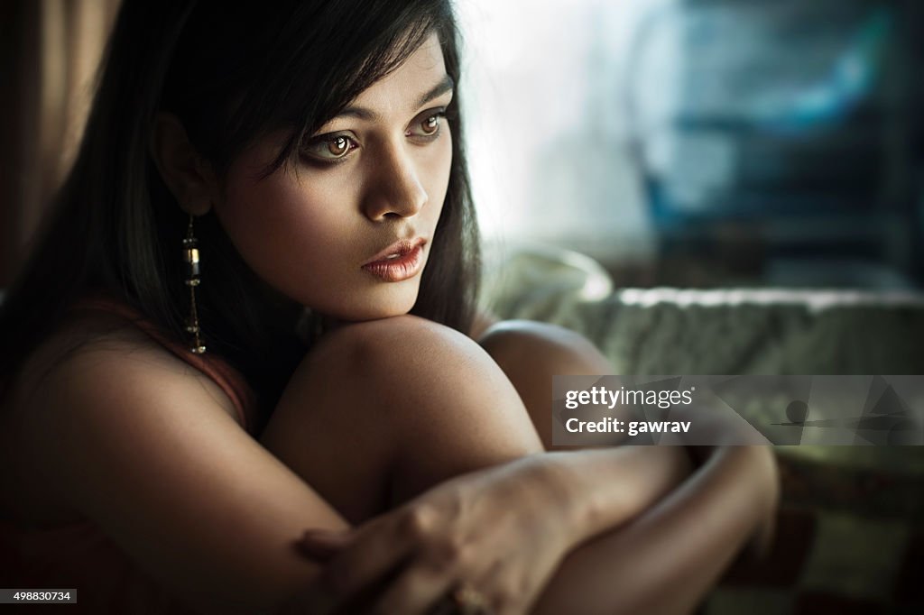 Close-up of serene Sad Asian teenager girl sitting near window.