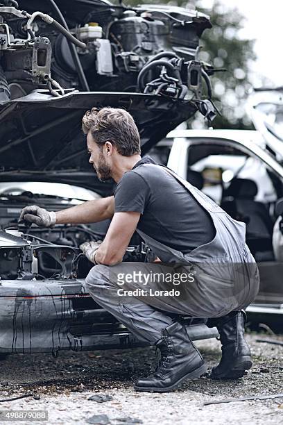 männliche mechaniker arbeiten am auto destroyed - autoschrottplatz stock-fotos und bilder