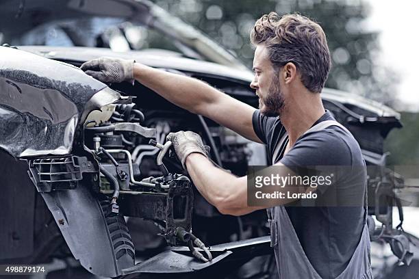 männliche mechaniker arbeiten am auto destroyed - autoschrottplatz stock-fotos und bilder