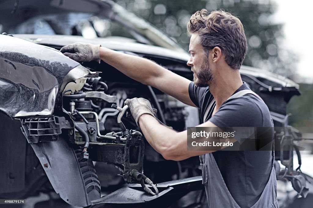 Hombre mecánico trabajando en coche destruido