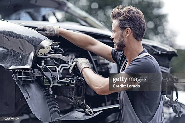 male mechanic working on destroyed car - junkyard stock pictures, royalty-free photos & images