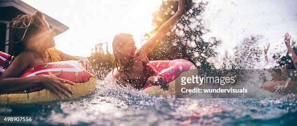teen friends splashing in a pool with colourful inflatables - swimming pool stock pictures, royalty-free photos & images