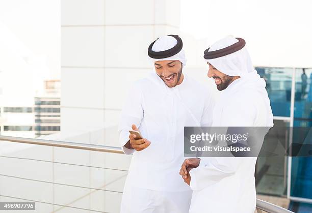 excited emirati men looking at content on the phone - emirati man portrait stockfoto's en -beelden