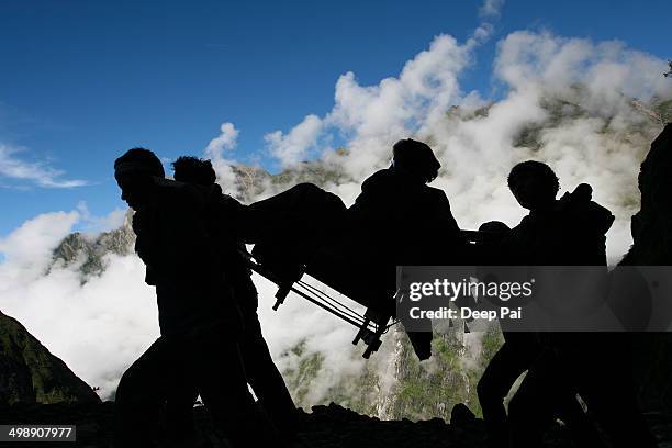 Silhouette of an old lady being carried in a chair by porters up the steep winding path to the Hemkund Sahib Gurudwara in the Himalayas. The temple...