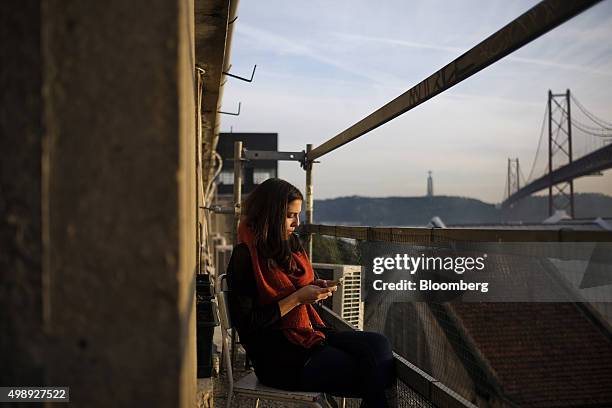 Tech entrepreneur sits and uses her smartphone with a view of 25th April bridge from the balcony of CoworkLisboa which provides office space for...