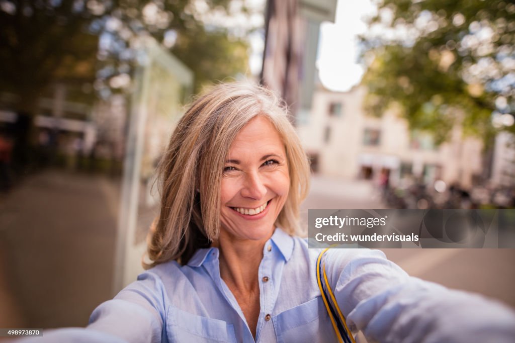 Sonriente mujer madura en una calle de la ciudad toma diversión autofoto