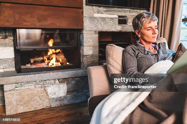 woman reading a book on the couch - haardvuur stockfoto's en -beelden